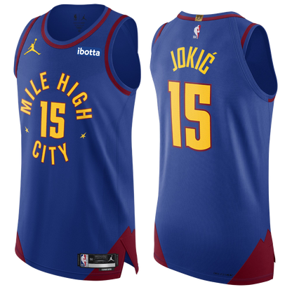 Royal Blue Nuggets Statement Jokic #15 Authentic Jersey. Has the Mile High City mantra across the chest with the #15 in the middle with yellow lettering surrounding by maroon lining. On the back neck tag, has the "1" in gold indicating our one NBA championship.
