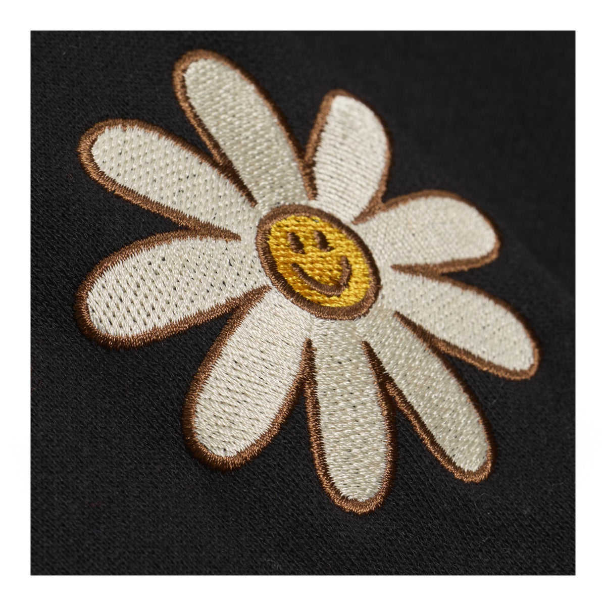 An embroidered daisy patch with cream petals, a yellow smiley face center, and brown outlines, shown on a black textured fabric background.