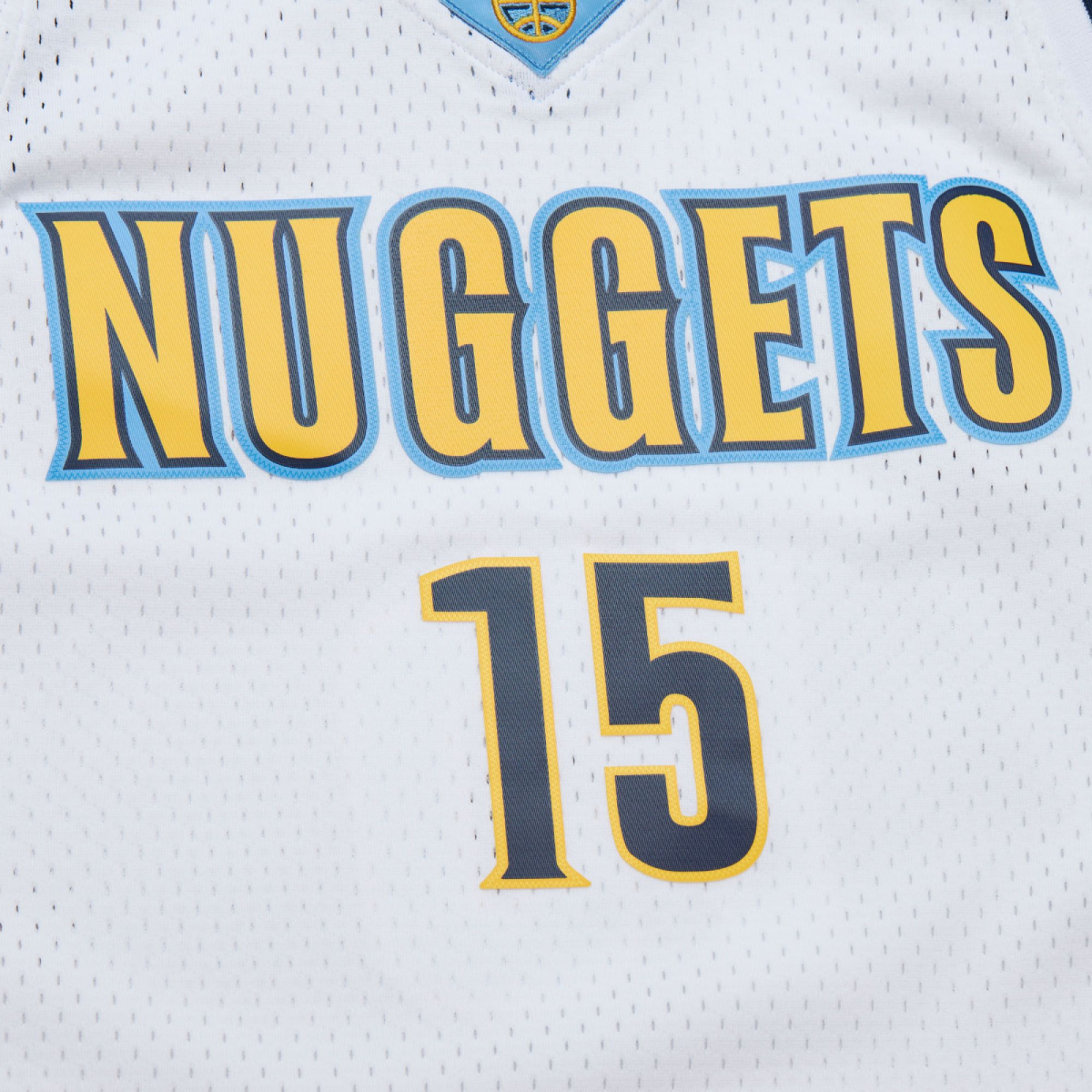 Up close view of front White basketball jersey with Nuggets in yellow with navy trim, trimmed in light blue and number '15' in navy with yellow outline on a white background